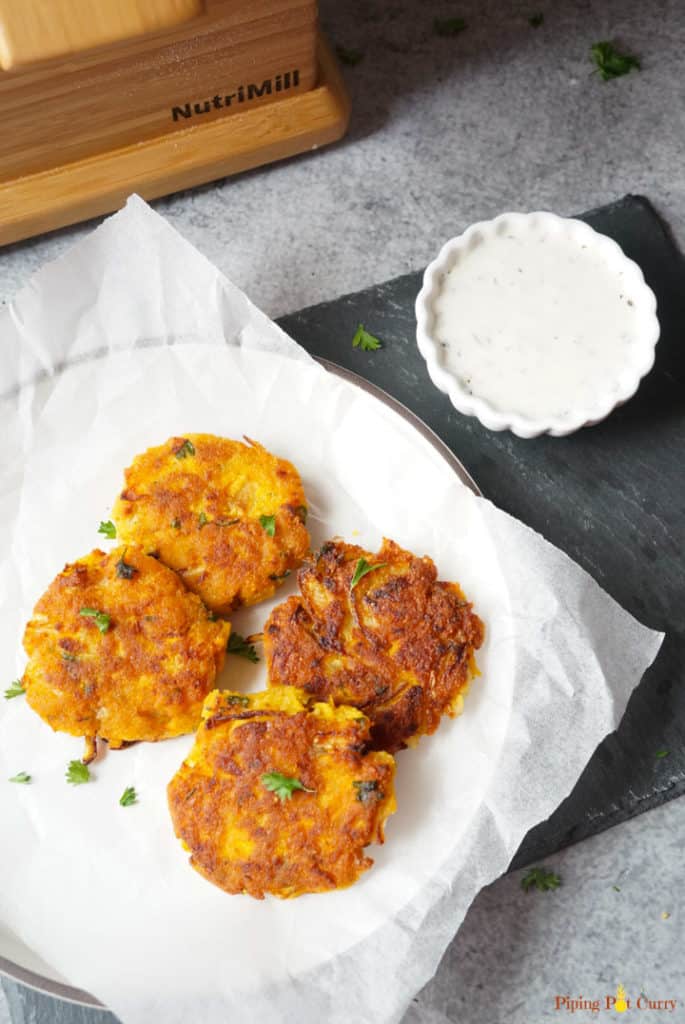 Try these super delicious and crunchy Chickpea Squash Fritters. These vegan & gluten free Chickpea Squash Fritters are so easy and take less than 30 minutes to make! Vegan Chickpea Squash Fritters in a plate with yogurt dip on the side and Nutrimill Harvest in the back