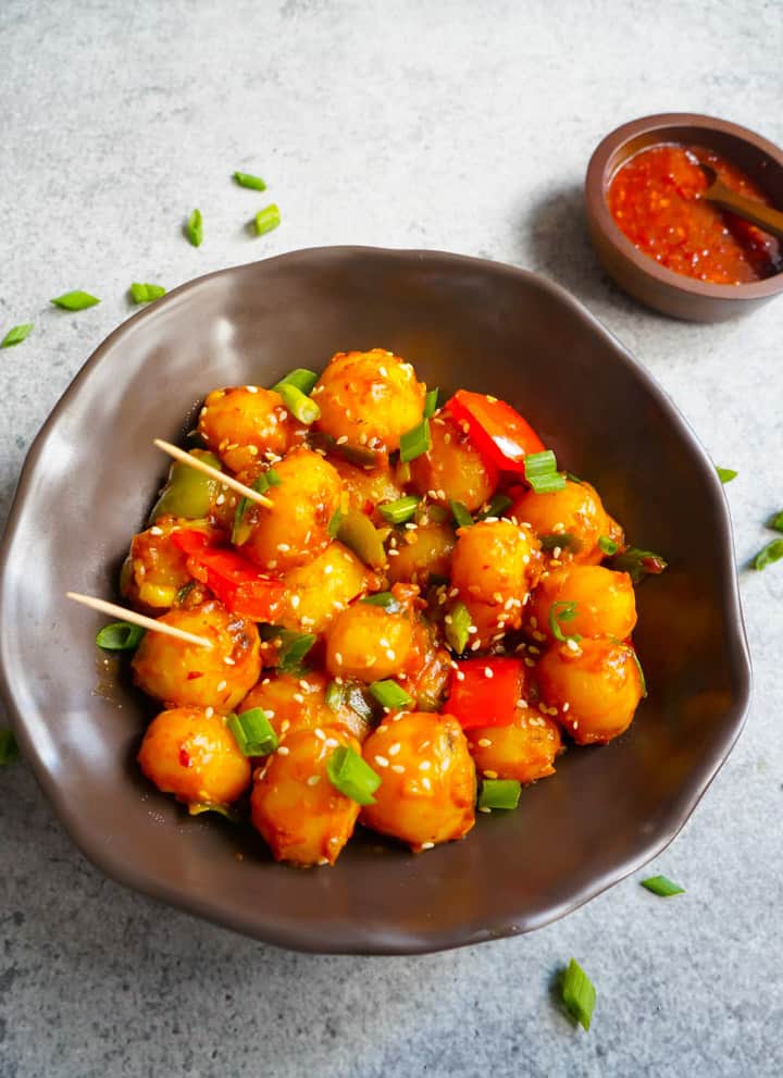 Flavorful and easy Garlic Chili Potatoes, made with steamed potatoes, garlic, chili sauce and honey, sprinkled with green onions and sesame seeds. Enjoy them as an appetizer or side! Garlic Chili potatoes in a bowl and chili sauce on the side