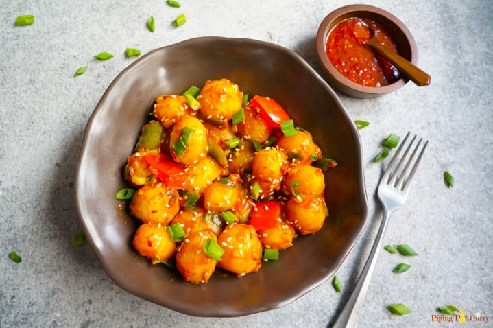 Flavorful and easy Garlic Chili Potatoes, made with steamed potatoes, garlic, chili sauce and honey, sprinkled with green onions and sesame seeds. Enjoy them as an appetizer or side! Garlic Chili potatoes in a bowl and chili sauce on the side