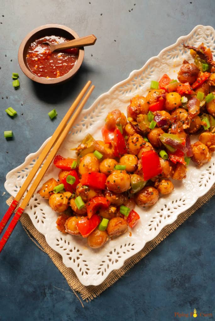 Flavorful and easy Garlic Chili Potatoes, made with steamed potatoes, garlic, chili sauce and honey, sprinkled with green onions and sesame seeds. Enjoy them as an appetizer or side! Garlicky Chili Potatoes - in a serving tray with chopsticks and chili sauce on the side
