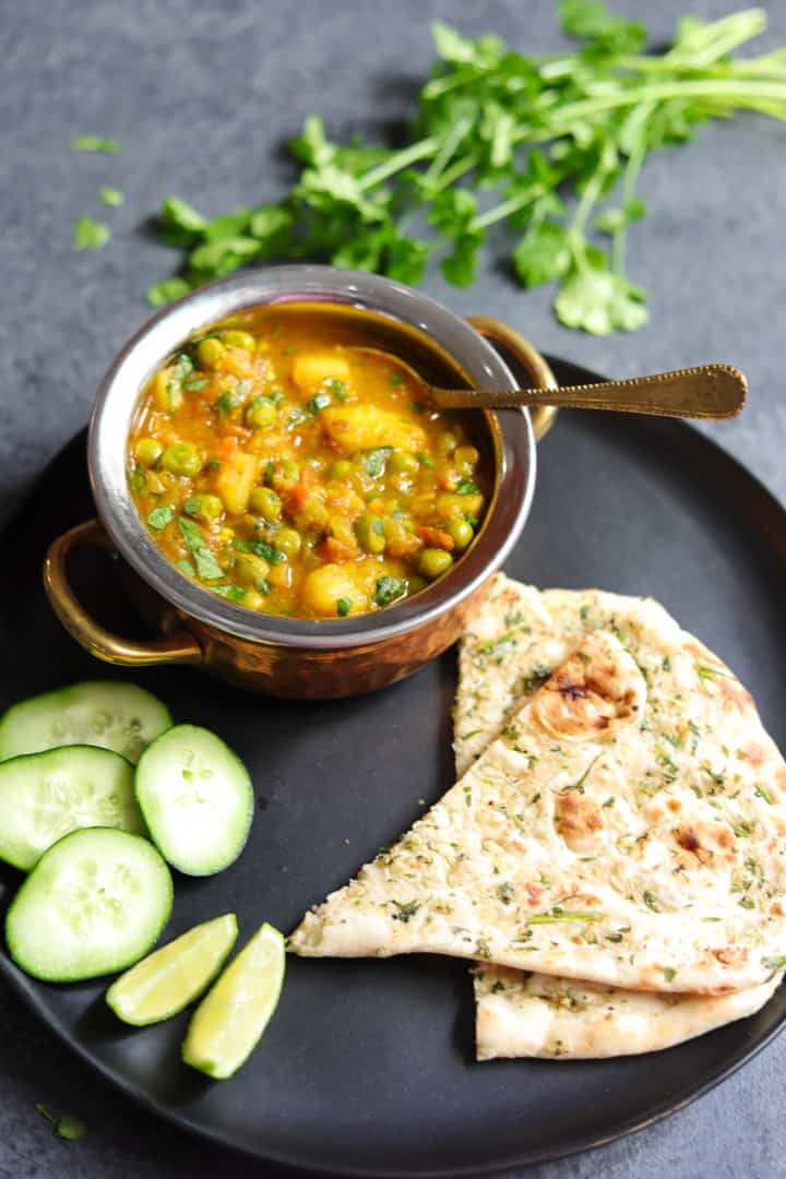 Aloo Matar is a quick and easy potatoes and peas curry, made in the Instant Pot or stovetop. This vegan and gluten free Aloo Matar Masala is perfect for a delicious warm weeknight dinner! #aloomatar #indian #curry #vegan #glutenfree #instantpot #pipingpotcurry | pipingpotcurry.com Aloo Matar made in instant pot served in a bowl, with naan bread on the side