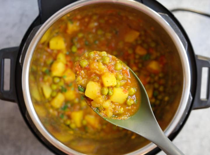 Aloo Matar is a quick and easy potatoes and peas curry, made in the Instant Pot or stovetop. This vegan and gluten free Aloo Matar Masala is perfect for a delicious warm weeknight dinner! #aloomatar #indian #curry #vegan #glutenfree #instantpot #pipingpotcurry | pipingpotcurry.com Aloo Matar in instant pot - perfectly cooked and shown in a ladle
