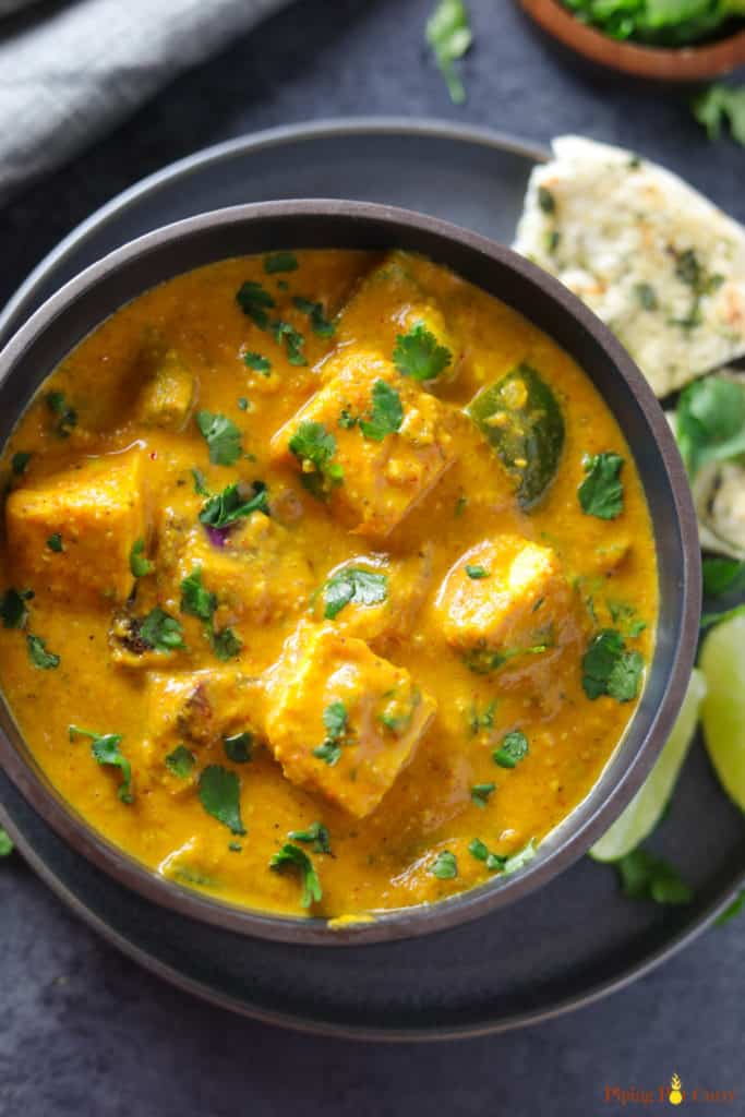 Paneer Tikka Masala is a flavorful and aromatic curry, made with marinated and grilled paneer cubes simmered in a rich onion tomato gravy along with warm spices. | #paneer #tikka #instantpot #pressurecooker #vegetarian #glutenfree #pipingpotcurry | pipingpotcurry.com Paneer Tikka Masala made in Instant Pot served in a bowl with some naan and limes on the side.