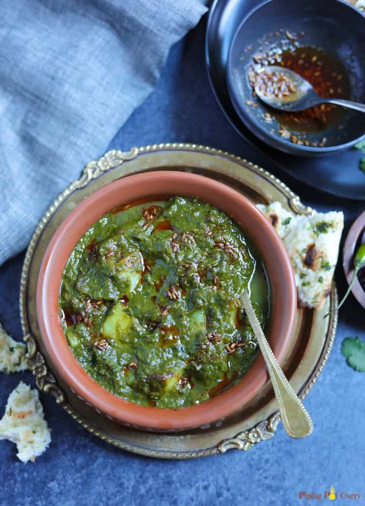 Saag Aloo made in the instant pot served in a earthen bowl with the tempering in the back and naan on the side.