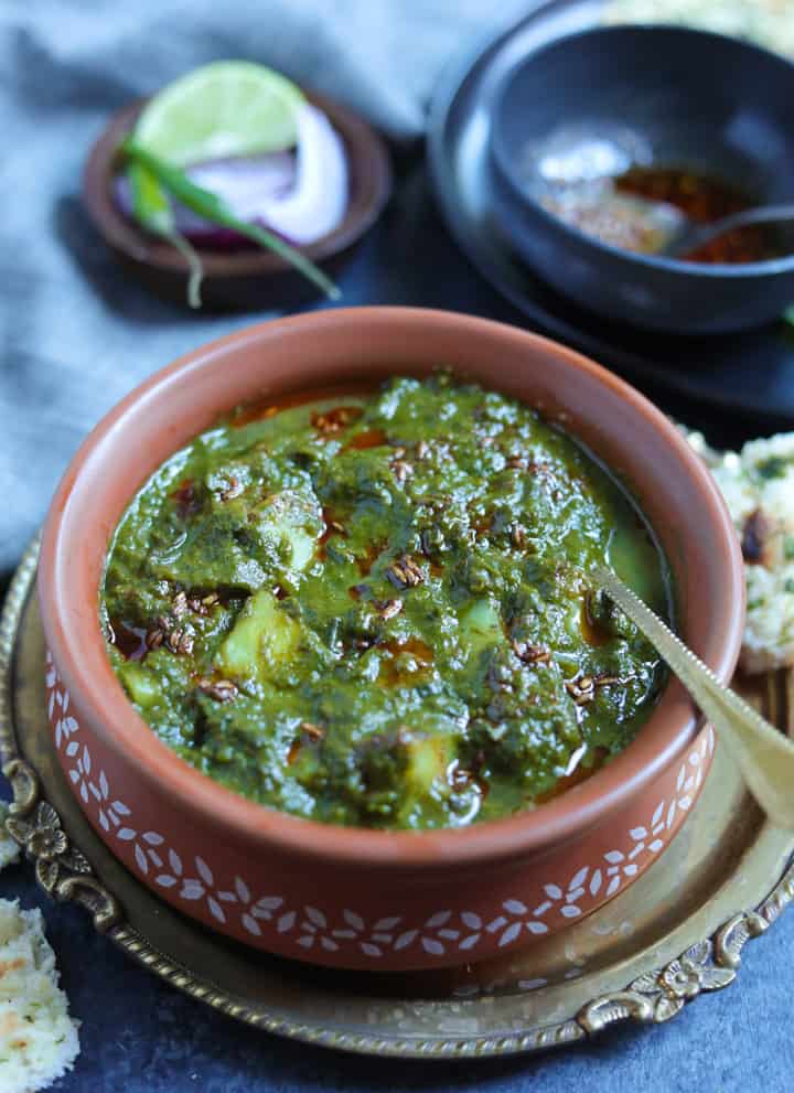 Saag Aloo made in the instant pot served in a earthen bowl with the tempering in the back and naan on the side.