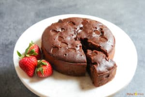 A whole brownie cake made in the instant pot, with a cut out piece and three strawberries