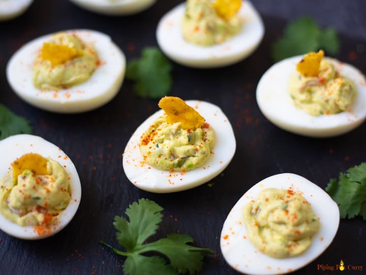 Guacamole Deviled Eggs on a black platter garnished with paprika and a tortilla chip