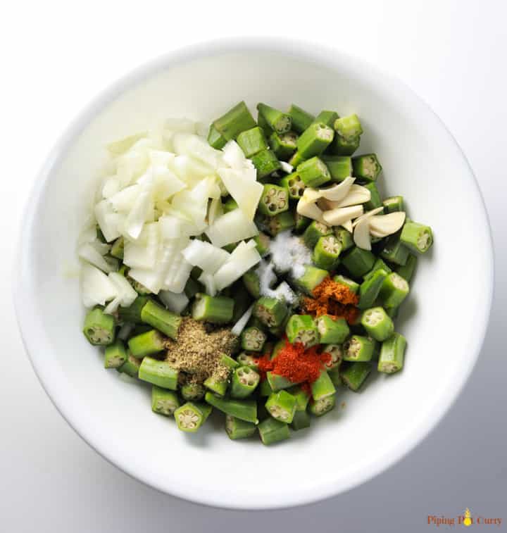 Ingredients to make Oven Roasted Okra with Onions in a white bowl, ready to be mixed.