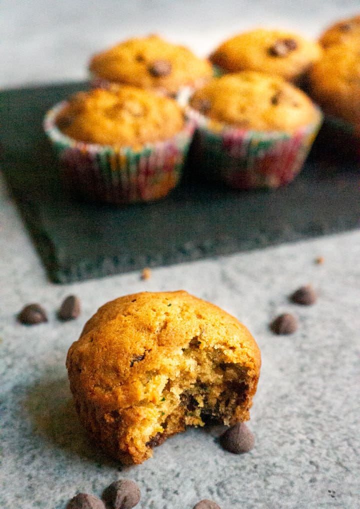 A bite taken from a Zucchini Chocolate Chip Muffins and more muffins on a serving platter in the back