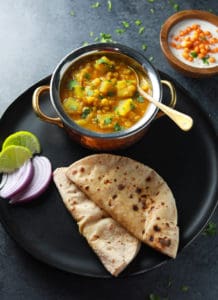 Lauki Chana Dal served in a black plate with roti, onions and lime.