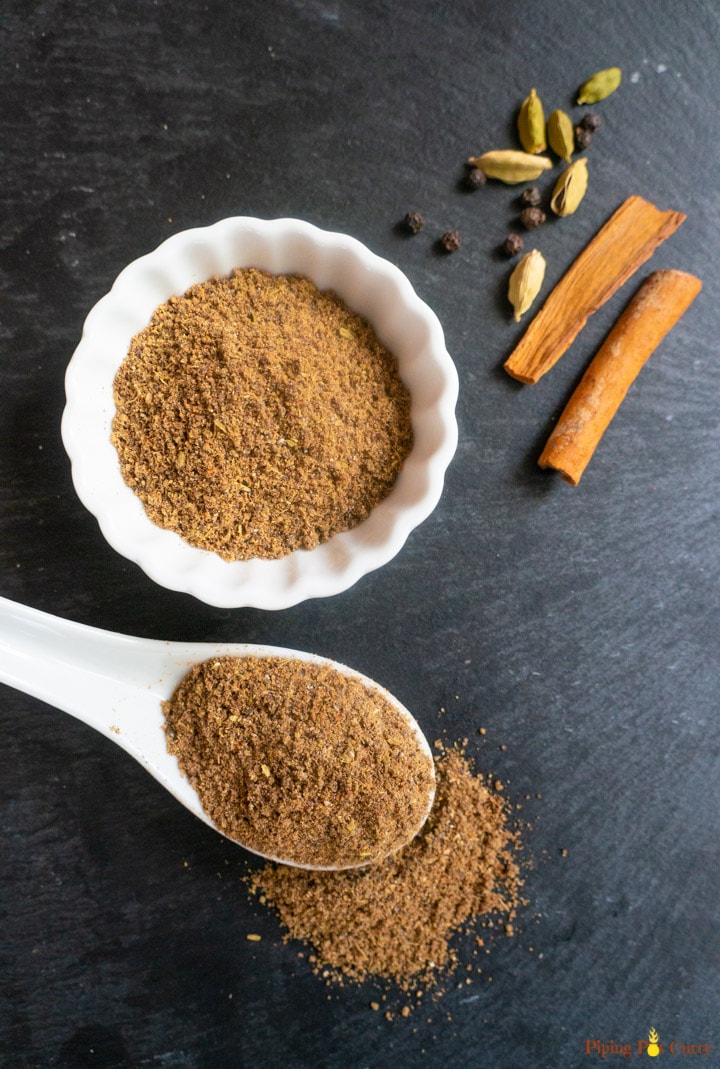 Chai Masala Spice Mix in a white bowl and spoon along with some whole spices
