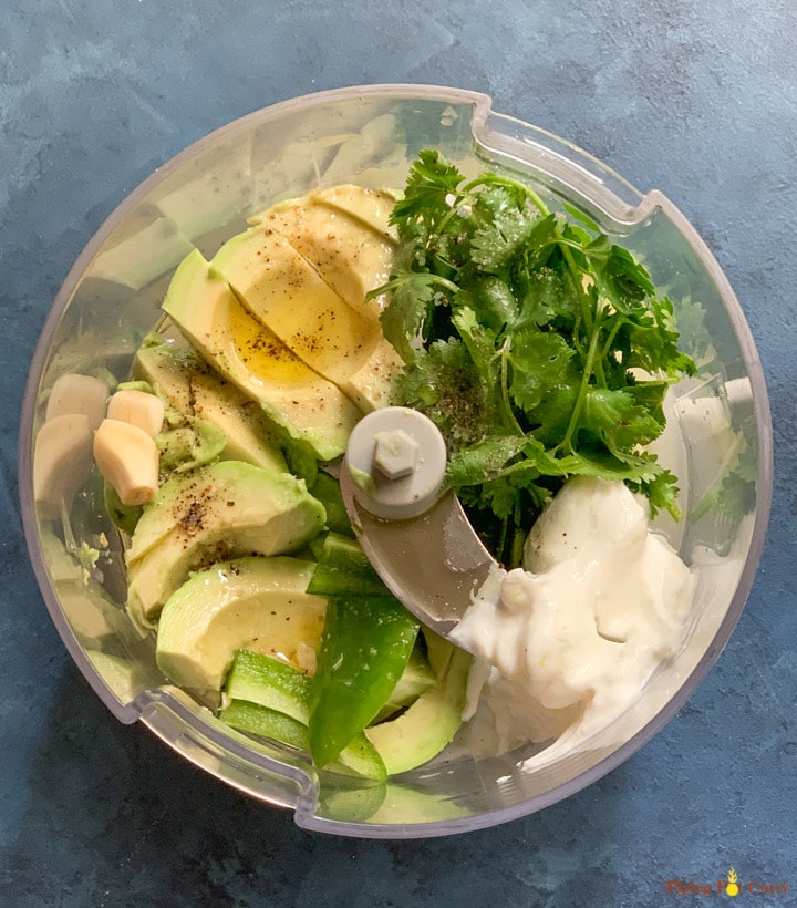 Ingredients such as avocado, cilantro, jalapeño and sour cream in a food processor.