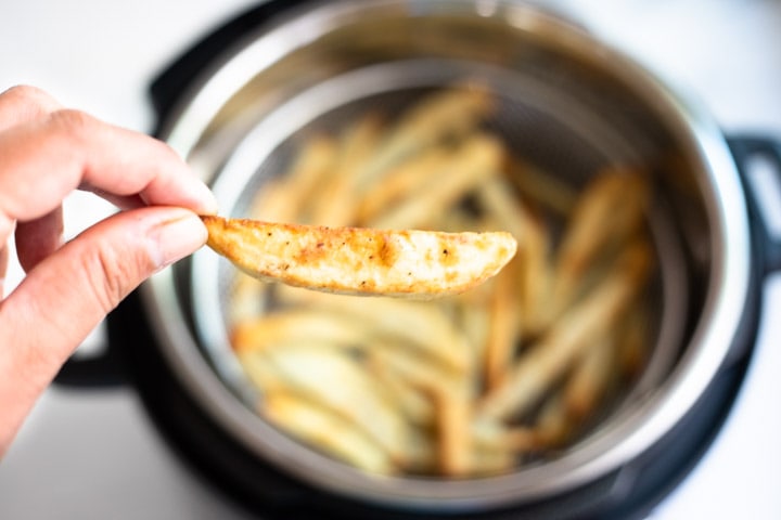 Close up of a crisped French fry, with pressure cooker in the background